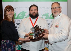 National Chef of Wales winner Josh Morris receives the dragon trophy from Minister for Rural Affairs Lesley Griffiths and Culinary Association of Wales president Arwyn Watkins, OBE.
